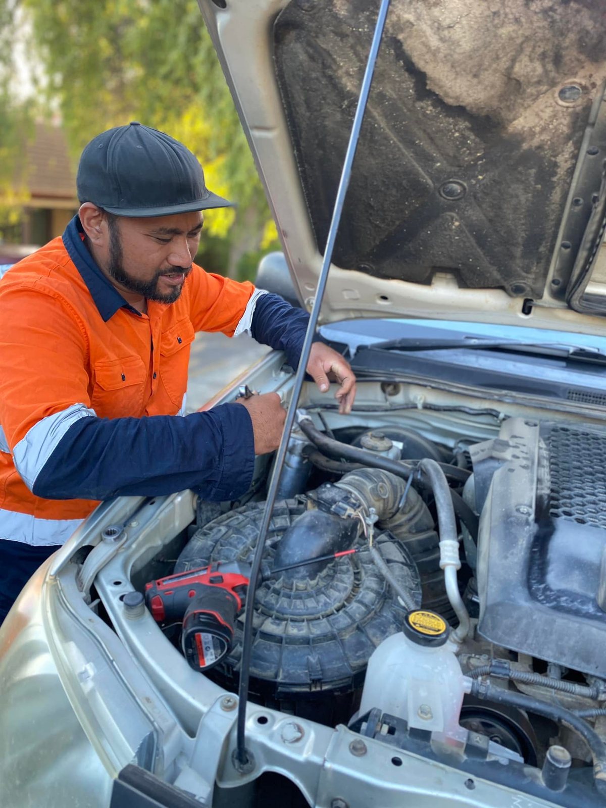 Froi in hi-vis workwear working under the bonnet of a car in a customer's driveway