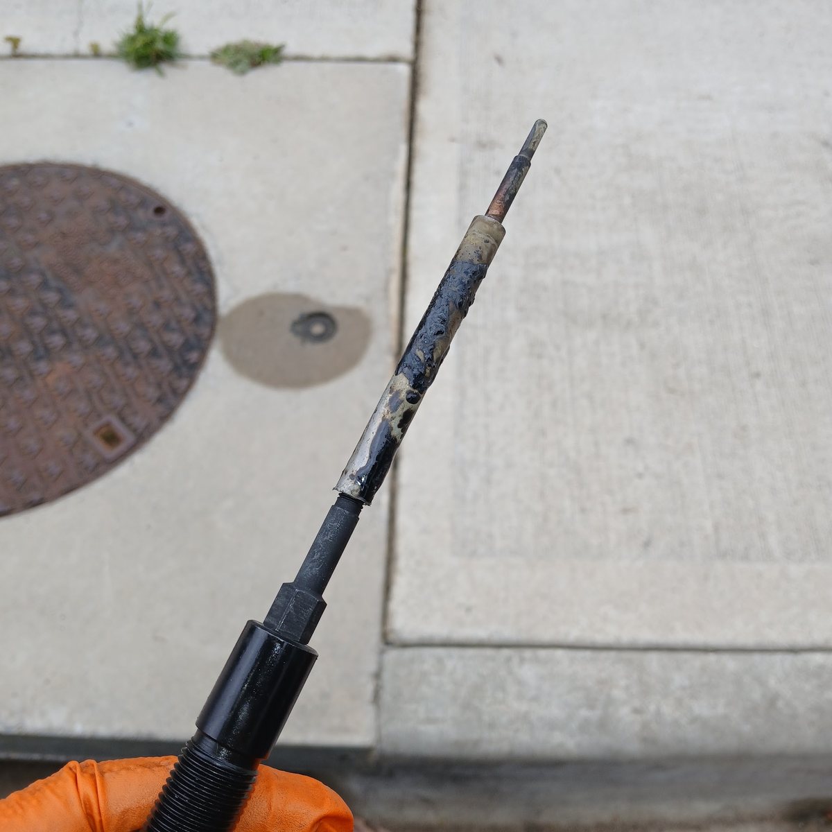 A worn, oil-coated engine part held up in an orange-gloved hand